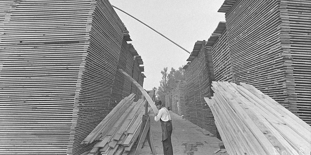 Lumber yard worker sorting through stacks of planks of wood