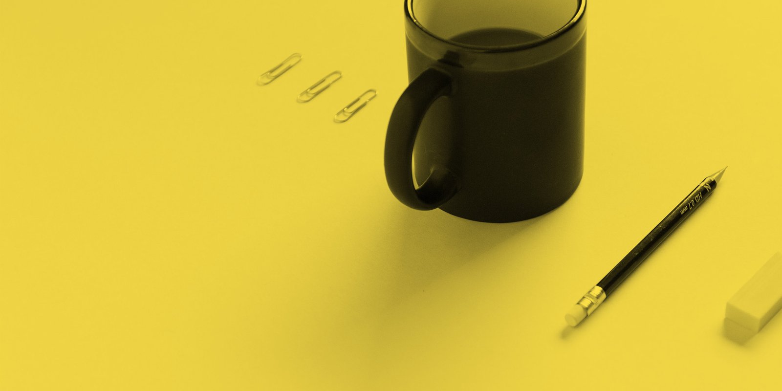 Three paper clips, a pencil, an eraser and a mug of coffee on an office desk
